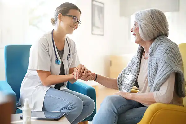 young female physician sitting with aged lady smiling